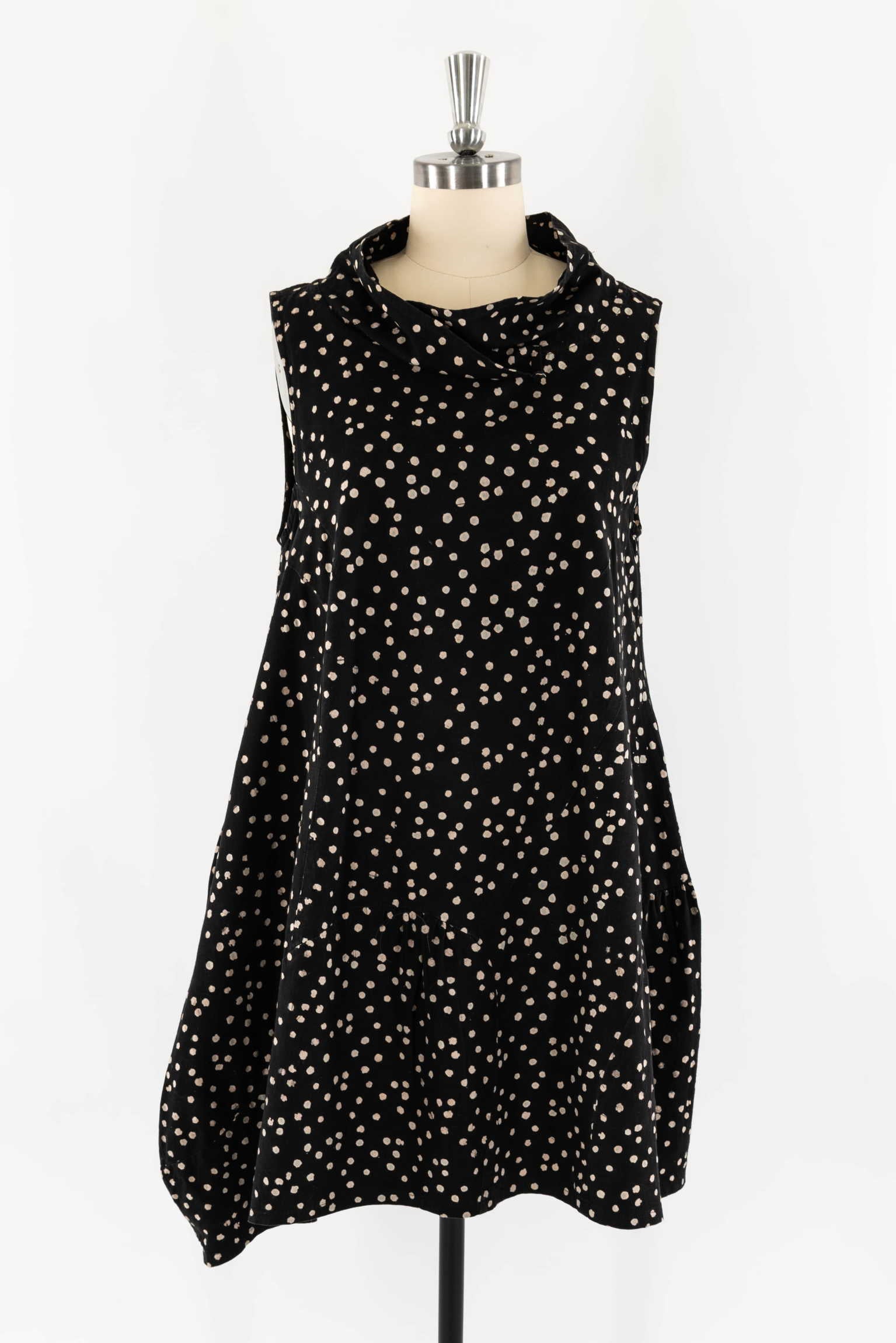 Black sleeveless dress with beige polka dots, cowl neck, and tiered hem on mannequin