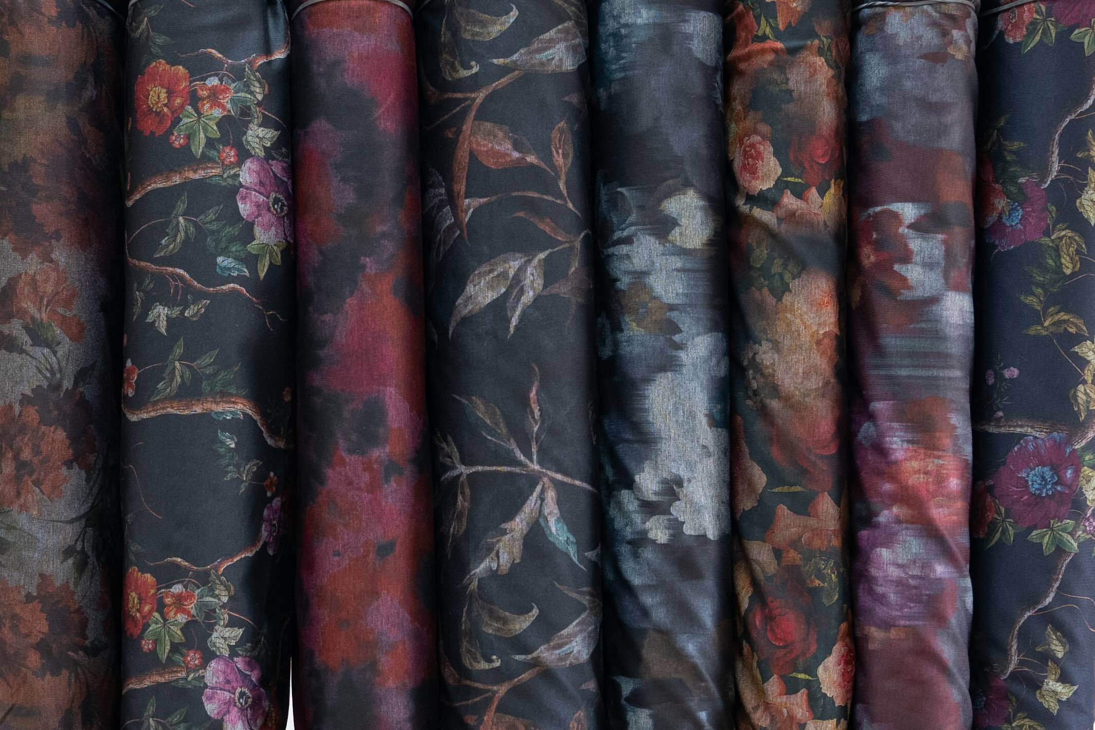 Rolls of dark floral and abstract printed fabric for apparel and quilting, featuring rich reds and botanical designs