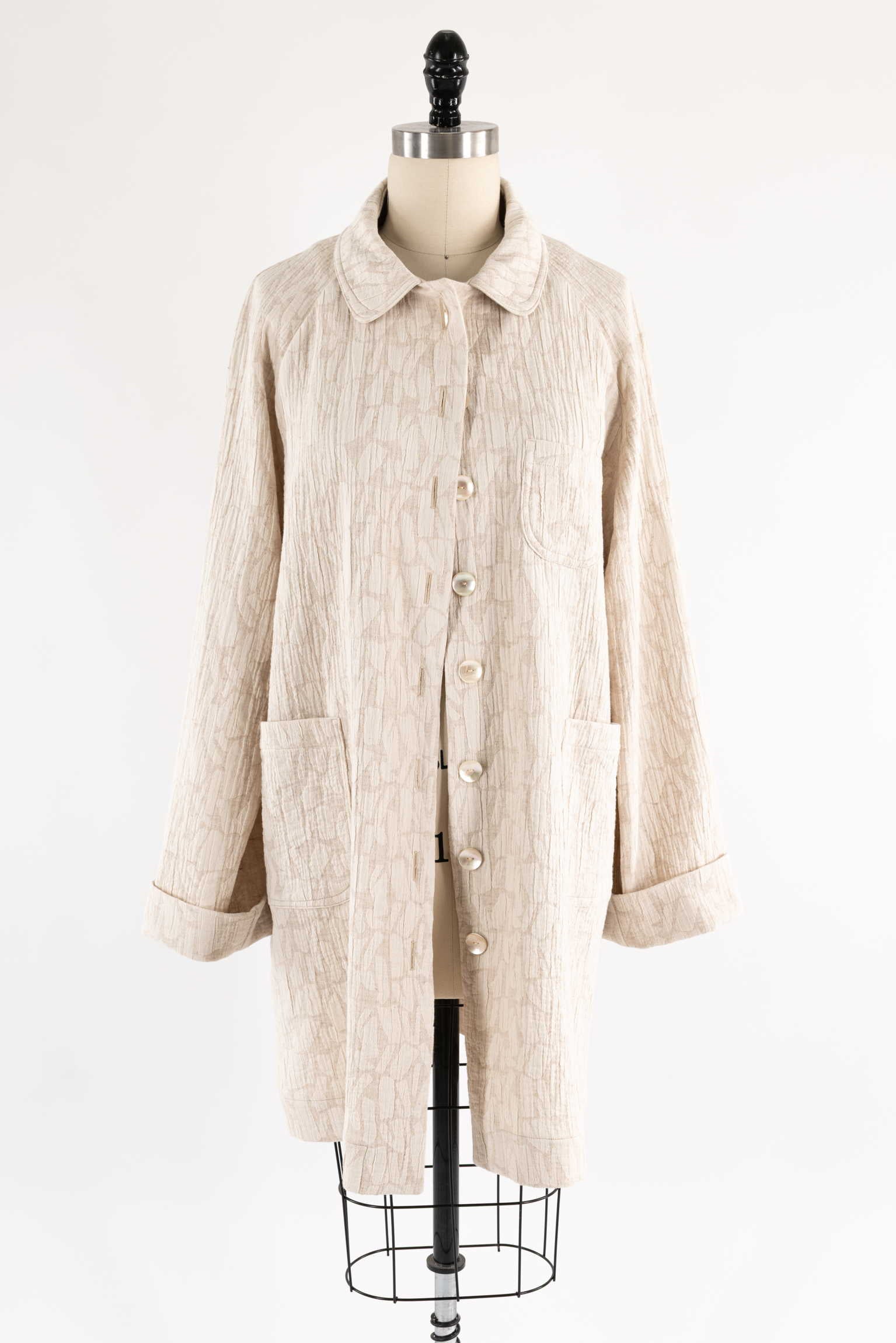 Beige textured button-up coat with collar and pockets on mannequin, ideal for sewing projects