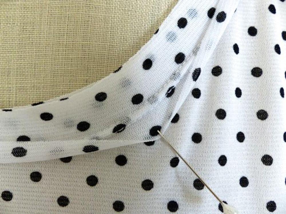White knit fabric with black polka dots, pinned for sewing, ideal for apparel and creative projects